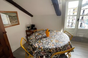 Un comedor con una mesa redonda, sillas amarillas, un mantel con estampado floral, un jarrón y vistas de edificios a través de una puerta.