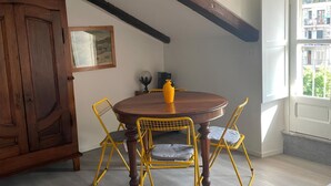 A dining area with a round wooden table, yellow chairs, a cabinet, and a window with a view.