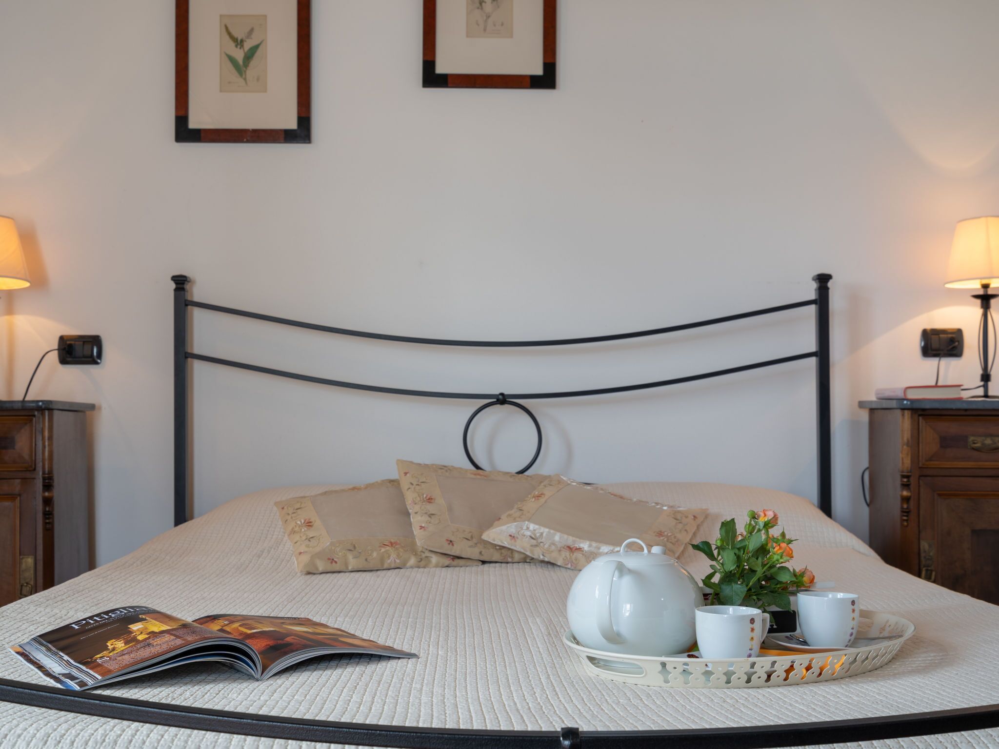 Una cama bien hecha con una bandeja de té, una revista y un arreglo floral.