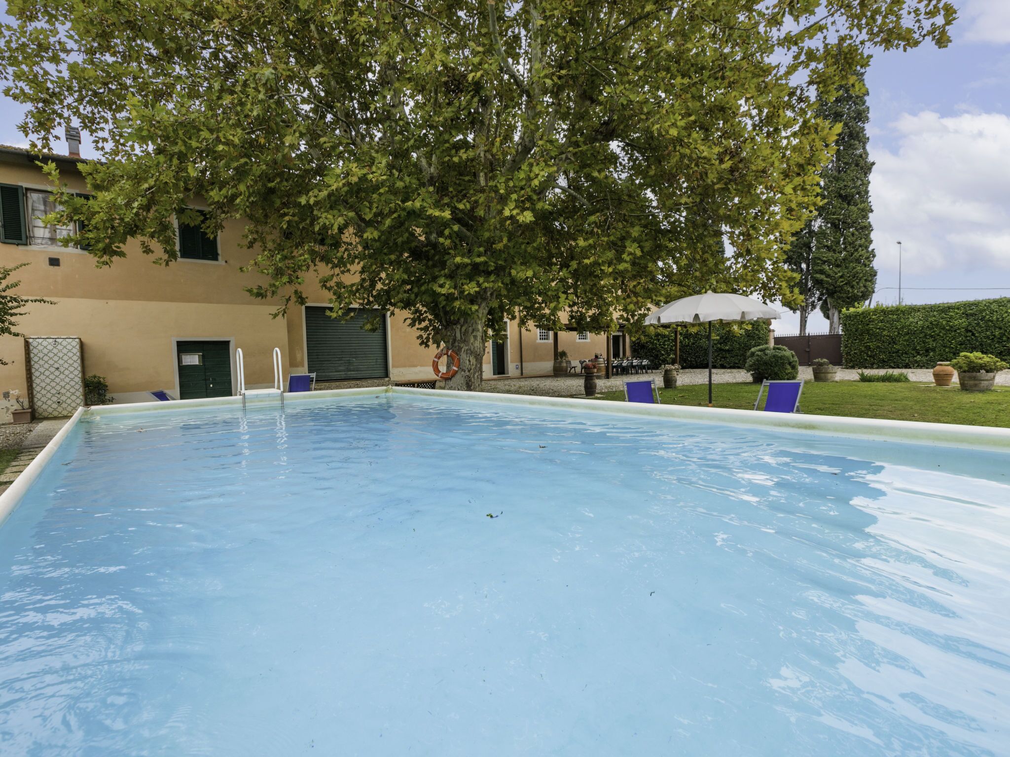 Une piscine avec une bouée de sauvetage, une chaise et un arbre en arrière-plan.