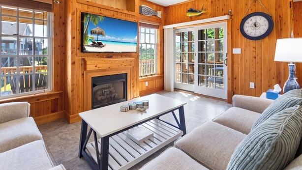 A cozy living room with wooden walls, a fireplace, a TV, and a view of the outdoors. - 3 br, dogs, canal front, sunrises/sunsets! (Avon)