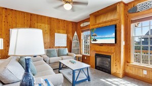 A living room with a sofa, coffee table, and TV. There is a fireplace and a window with a view. - 3 br, dogs, canal front, sunrises/sunsets! (Avon)