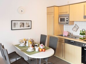 A compact kitchen with a microwave, sink, and a dining area with chairs and a table set for breakfast. - Strandvilla (LUB111) by Interhome (Ostseebad Lubmin)