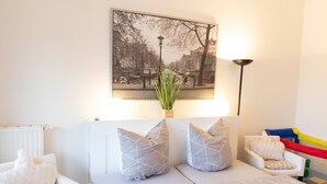 A modern hotel room with a bed, a chair, a sofa, a lamp, and a wall-mounted picture of a cityscape. - Strandvilla (LUB110) by Interhome (Ostseebad Lubmin)