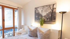 A bedroom with a bed, a window with curtains, a plant, and a cityscape painting. - Strandvilla (LUB110) by Interhome (Ostseebad Lubmin)
