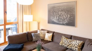 A living room with a brown sofa, a wooden coffee table with fruit, and a cityscape painting. - Strandvilla (LUB110) by Interhome (Ostseebad Lubmin)