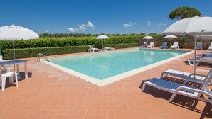 A swimming pool with white lounge chairs and umbrellas, surrounded by a brick patio and a hedge. - Podere Tre Termini by Interhome (Cecina)