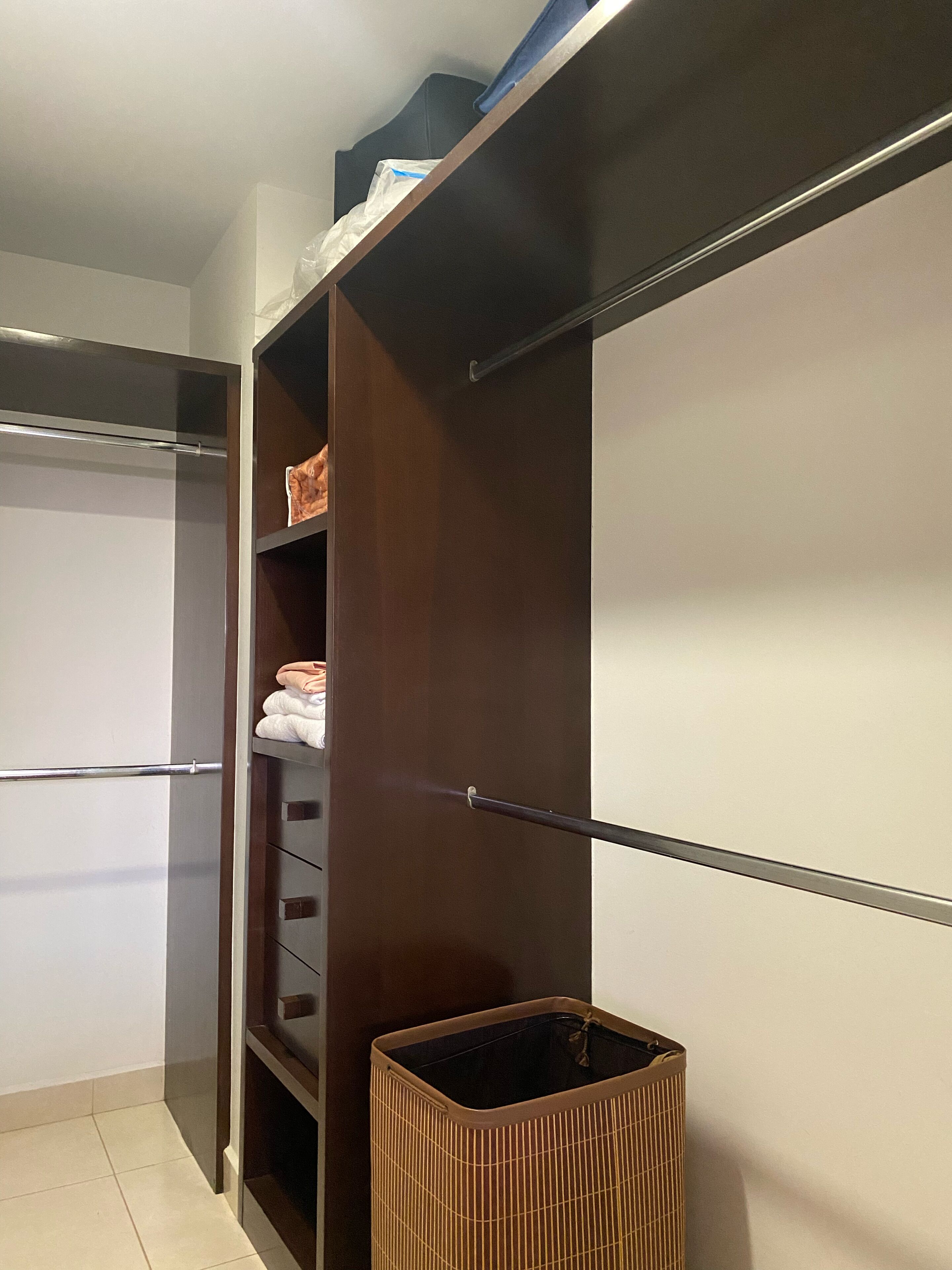 Un dressing avec une tringle à vêtements munie d’un miroir, une autre tringle pour suspendre les vêtements et un meuble de rangement avec des étagères.