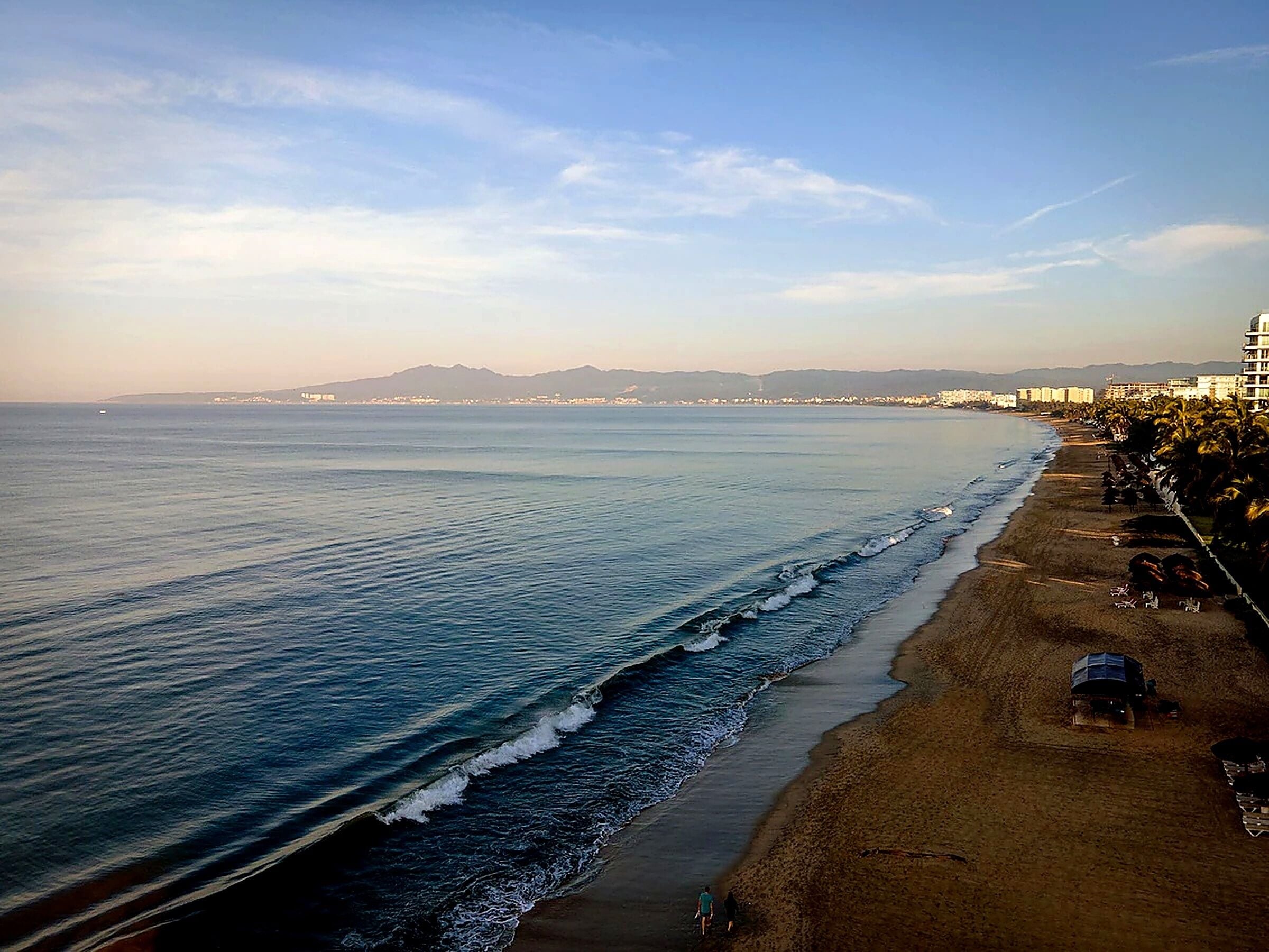 A coastal beach with a long stretch of sand, waves, and a distant cityscape.