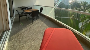 Un balcon avec une table et des chaises, un ventilateur de plafond et une vue sur les palmiers et les immeubles.