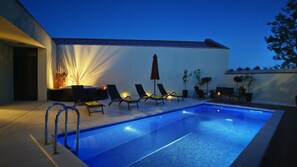 A swimming pool with lounge chairs and a table, surrounded by a white wall and plants.