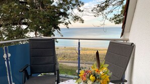 Un balcon avec deux chaises et une table recouverte d’une nappe à pois, donnant sur une plage et la mer.