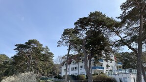 Un grand immeuble à étages, doté d’une façade blanche et agrémenté de touches de bleu, entouré d’une végétation luxuriante et d’arbres.