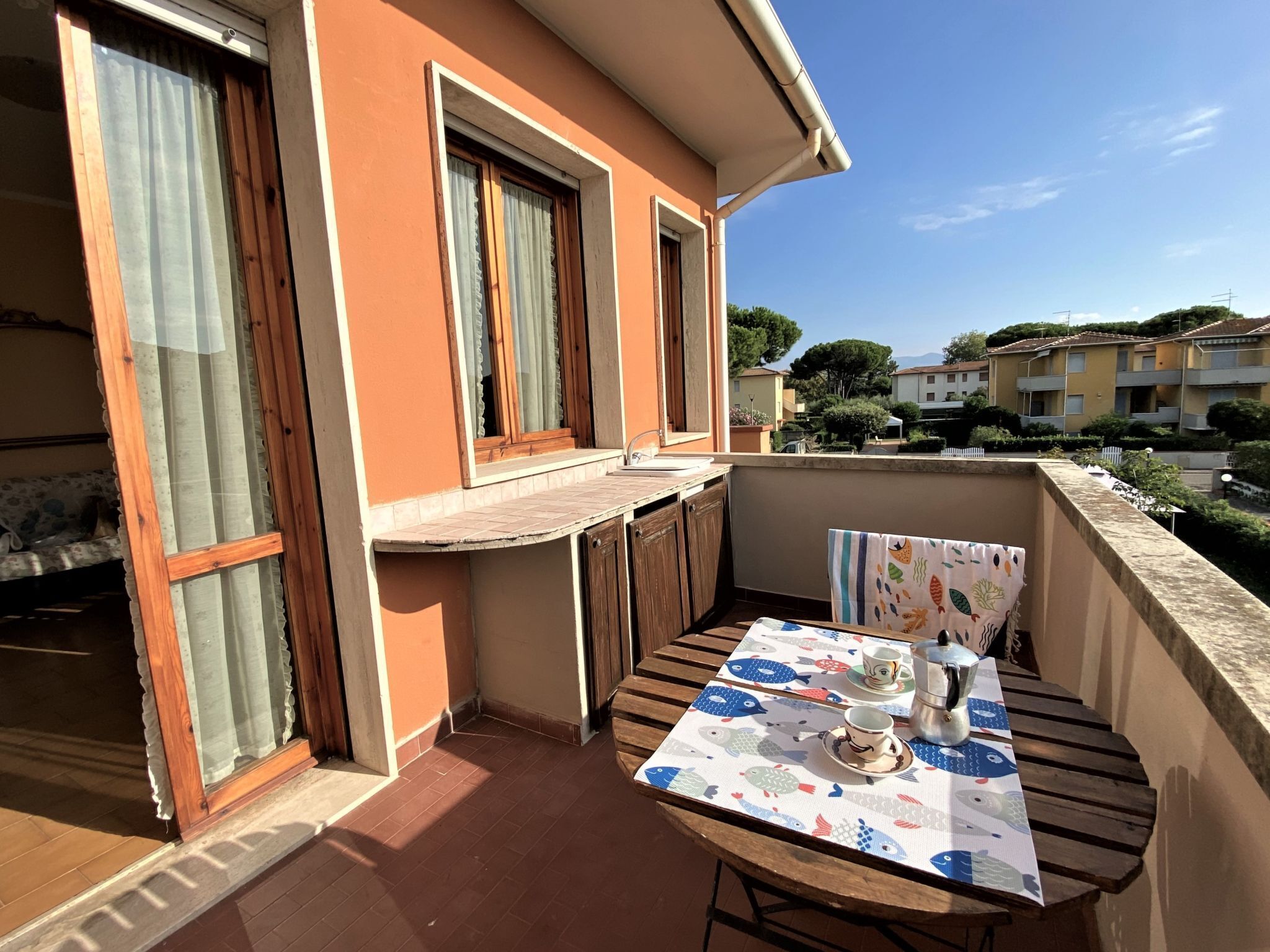 A balcony with a table set for two, a window, and a view of neighboring buildings.