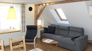 En hyggelig stue med en grå sofa, en træstol, et lille bord og et ovenlysvindue.