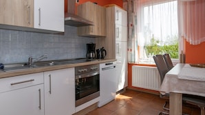 A modern kitchen with white cabinets, a stainless steel range hood, a built-in oven, and a window with curtains.