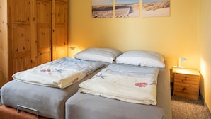 A bedroom with two beds, wooden wardrobe, and three wall-mounted pictures.
