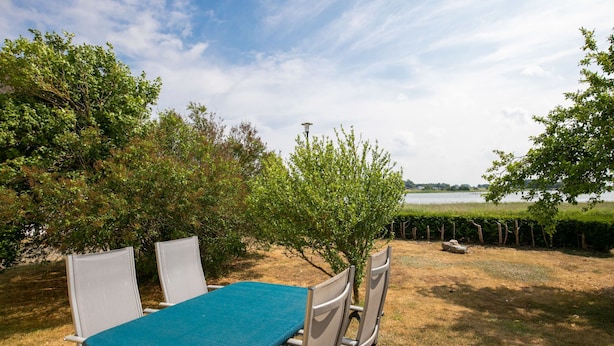 An outdoor seating area with a table and chairs, a view of a lake, and a grassy area with trees.