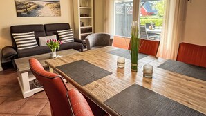 Ein modernes Wohnzimmer mit einem Holzesstisch, roten Stühlen, einer Couch mit gestreiften Kissen, einem Bücherregal und einem Gemälde einer Strandansicht.