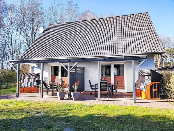 Une maison avec un toit en tuiles, une véranda couverte avec des chaises et des tables, et un jardin clos.