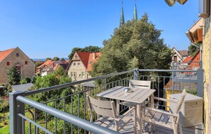 A balcony with a table and chairs, overlooking a town with traditional buildings and a church spire. - Stunning apartment in Quedlinburg (Quedlinburg)