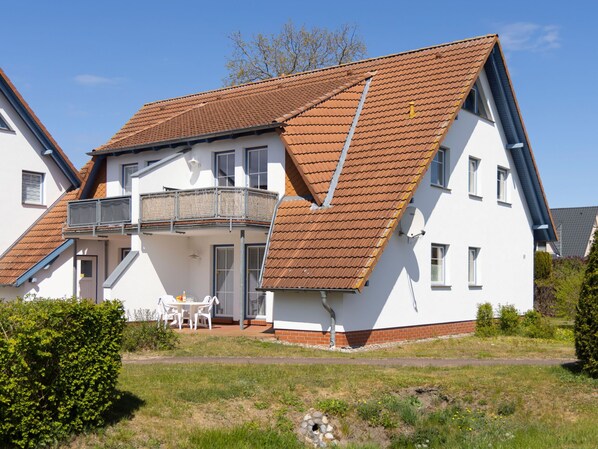 A two-story house with a sloped roof, a balcony, and a small garden area.