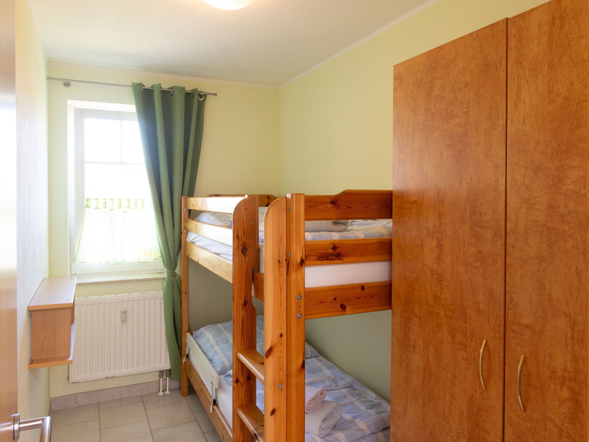 A bunk bed room with a wooden wardrobe and a window with curtains.