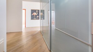 Un couloir doté d’un plancher en bois, d’une cloison en verre et d’une œuvre d’art encadrée représentant des flamants roses.