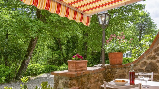 Un mur de pierre avec une table et des chaises, entouré de verdure et de plantes en pot.