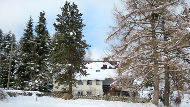 Une maison entourée d’arbres couverts de neige et d’une clôture.