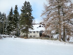 Ein Haus, umgeben von schneebedeckten Bäumen und einem Zaun.