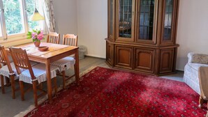 A dining area with a wooden table, chairs, a red patterned rug, and a wooden cabinet with glass doors. - Blechnerhof by Interhome (Feldberg)