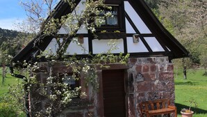 Une maison traditionnelle à colombages, avec des fondations en pierre, une porte en bois et un banc à l’extérieur.