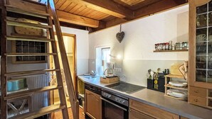 Une cuisine avec des meubles de rangement en bois, une cuisinière, un lave-vaisselle et une échelle appuyée contre le mur.