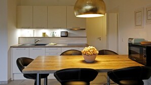 A modern kitchen with white cabinets, a wooden dining table, black chairs, and a large pendant light. - Am Weinberg by Interhome (Bad Dürkheim)