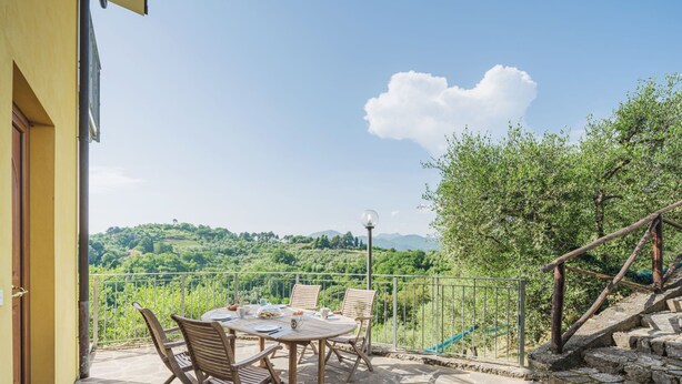 Eine Terrasse mit Tisch und Stühlen, ein Steinboden und Blick auf grüne Hügel.