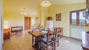 A dining area with a wooden table and chairs, a white refrigerator, and a window with a view of the countryside.