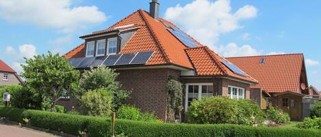 Una casa con techo de tejas rojas, paneles solares y fachada de ladrillo.