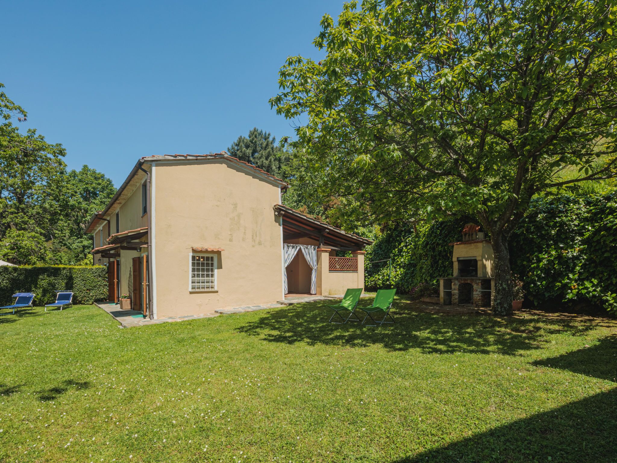 A two-story house with a patio, a small garden, and a tree.