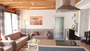 Un salon moderne comprenant un ensemble de canapés, une table basse et un coin cuisine avec une cuisinière et des placards.