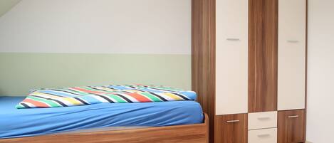 A bedroom with a bed, a wooden wardrobe, and a small drawer unit.