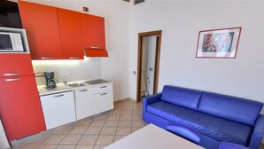 A compact kitchen with red cabinets, a white countertop, and a blue sofa in a living area.