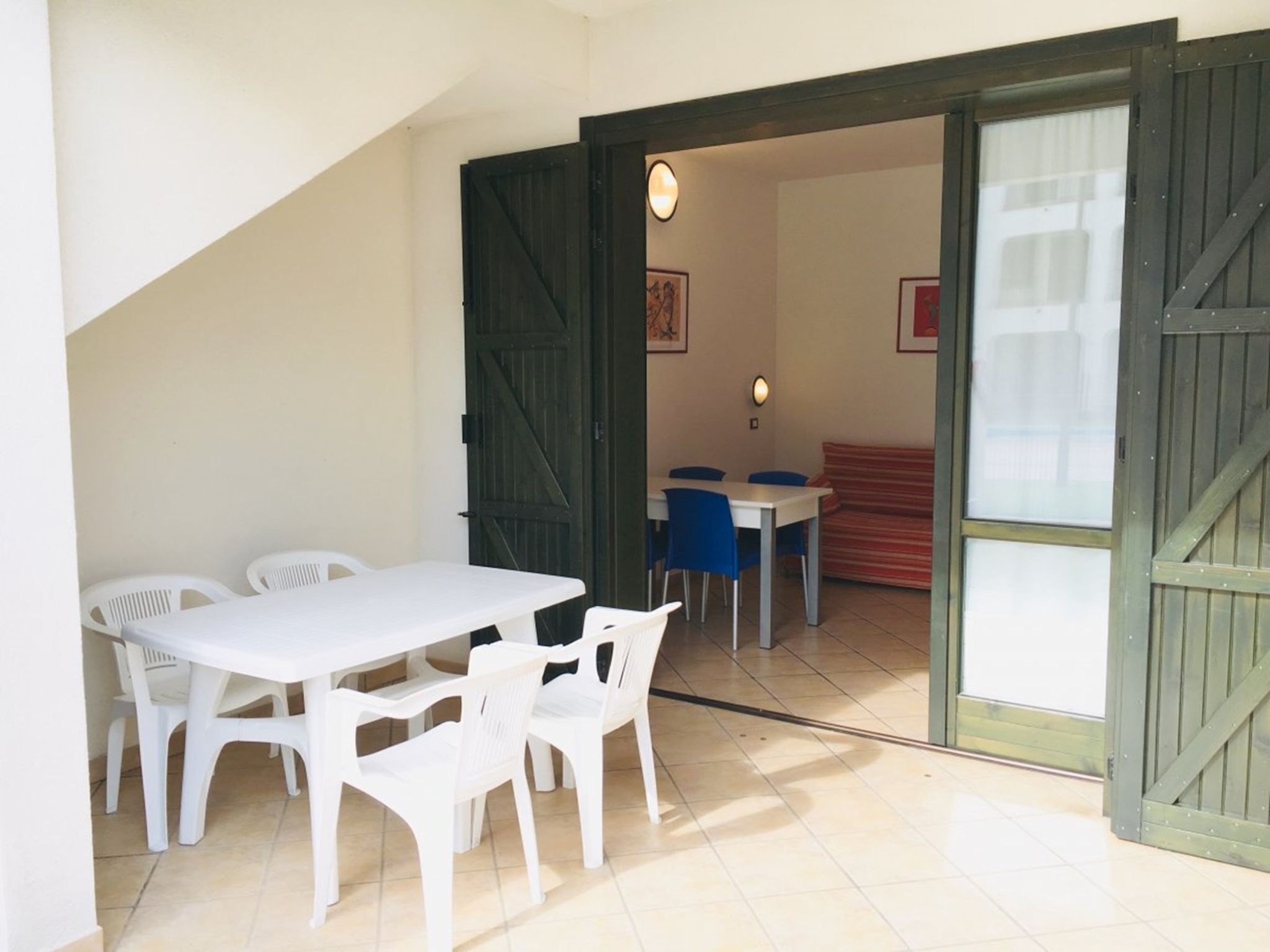 A dining area with a white table and chairs, a red sofa, and a view through a wooden door.
