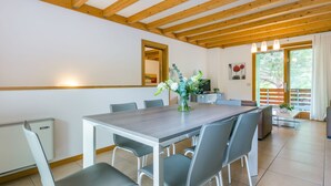 Un comedor moderno con techo de madera, una mesa grande, sillas grises y un jarrón de flores.
