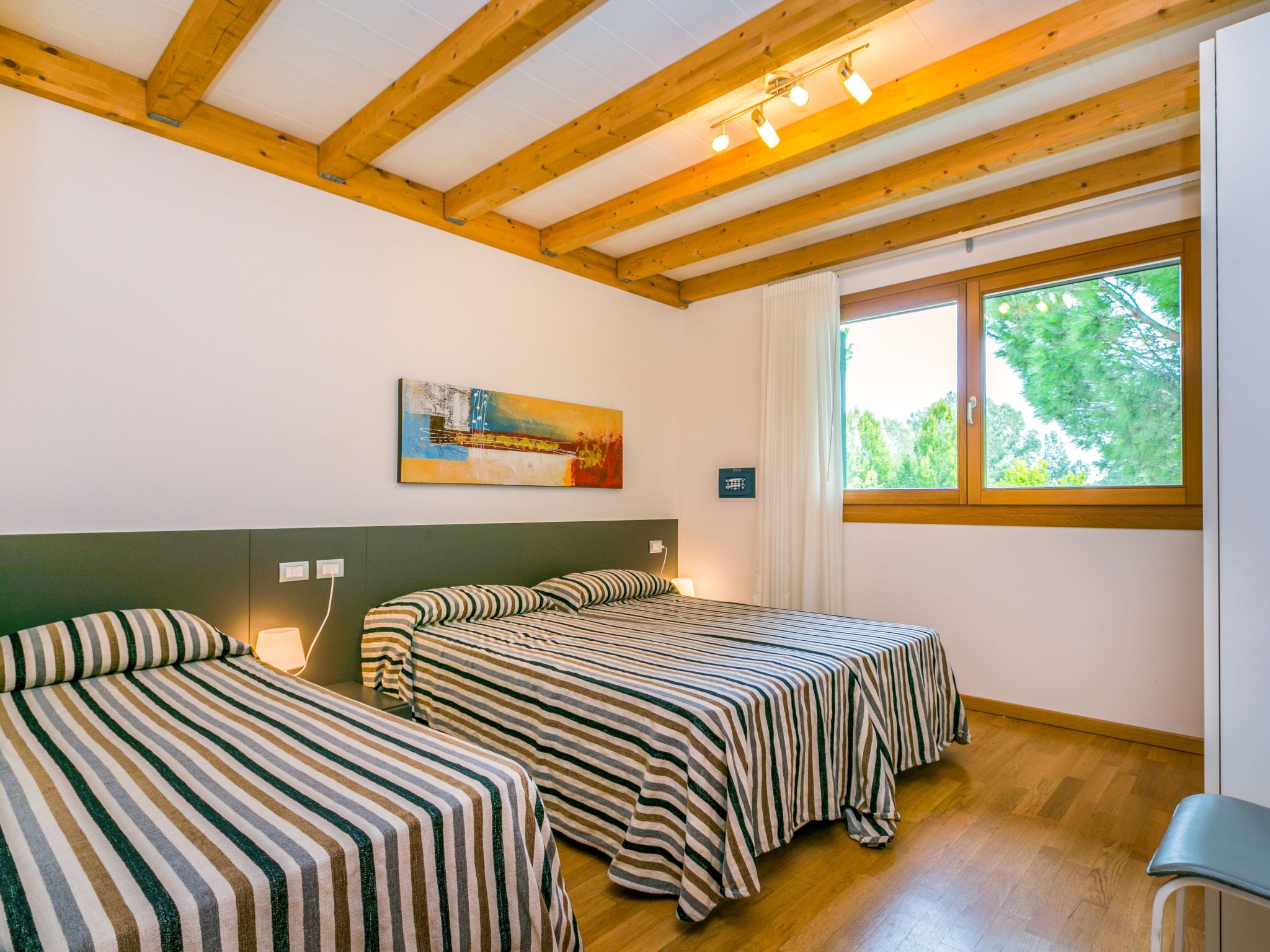 Ein Zimmer mit zwei Betten, Holzbalken, einem Gemälde, einem Fenster und einem Stuhl.