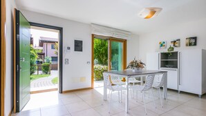 Una cocina moderna con armarios blancos, una mesa de comedor con sillas y vista a un jardín a través de una puerta corrediza de vidrio.