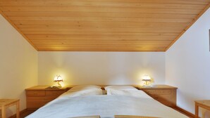 A bedroom with a wooden ceiling, two bedside tables with lamps, a bed with a white bedspread, and a wooden nightstand with a book. - Apartment Tirol by Interhome (Ortisei St Ulrich)