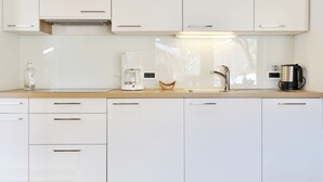 A modern kitchen with white cabinets, a coffee maker, a kettle, and a sink. - Apartment Tirol by Interhome (Ortisei St Ulrich)