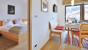 A room with a bed, a small table with chairs, a television, and a window with a view of buildings. - Apartment Tirol by Interhome (Ortisei St Ulrich)