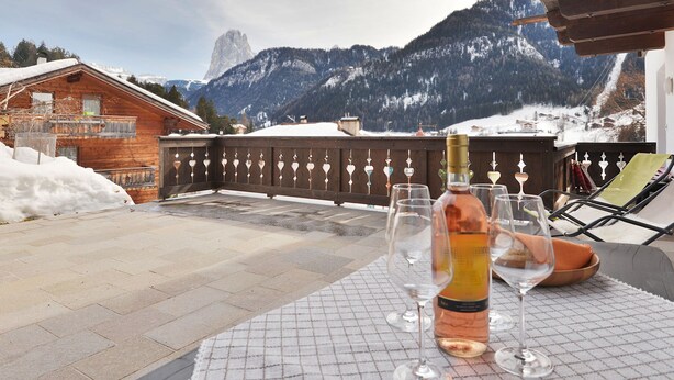 A terrace with a table set for a meal, overlooking a mountainous landscape with a wooden cabin and a snow-covered mountain. - Apartment Tirol by Interhome (Ortisei St Ulrich)
